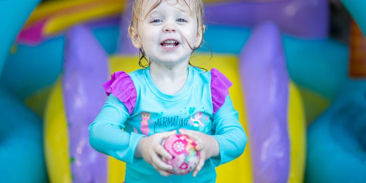 A little girl holding a pink ball in an indoor play center.