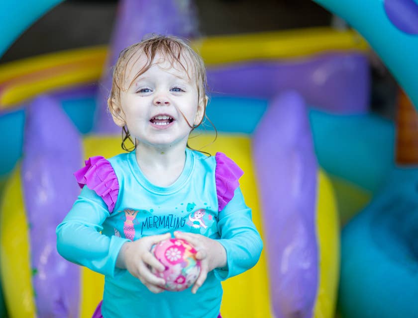 Une petite fille tenant un ballon rose dans une aire de jeux intérieure.