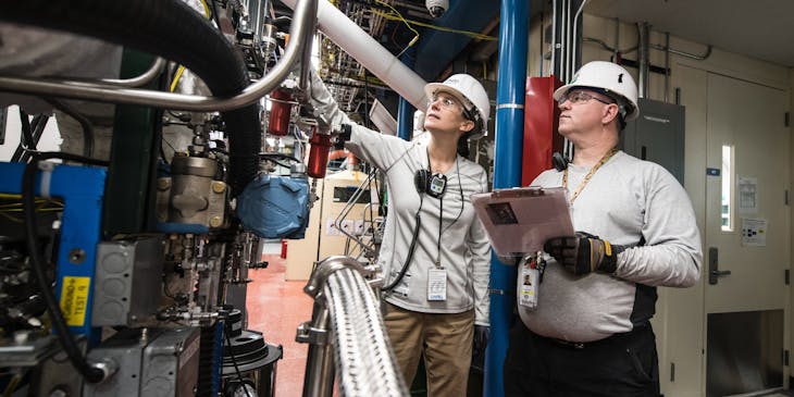 Two people inspecting heavy machinery inside a facility.
