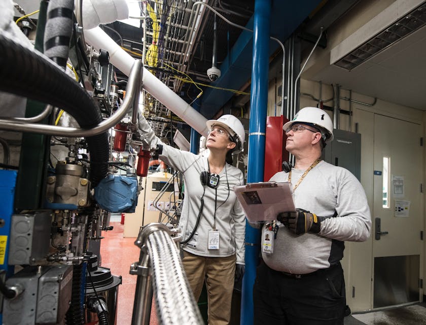 Two people inspecting heavy machinery inside a facility.