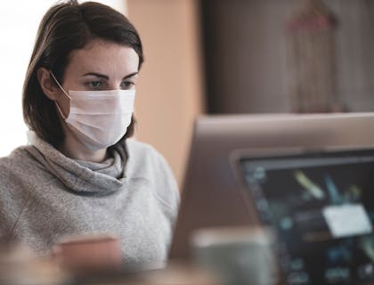 Infectious disease specialist wearing a mask and sitting behind a computer screen.