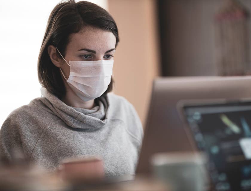 Uma especialista em doenças infecciosas com uma máscara no rosto sentada atrás de uma tela de computador.