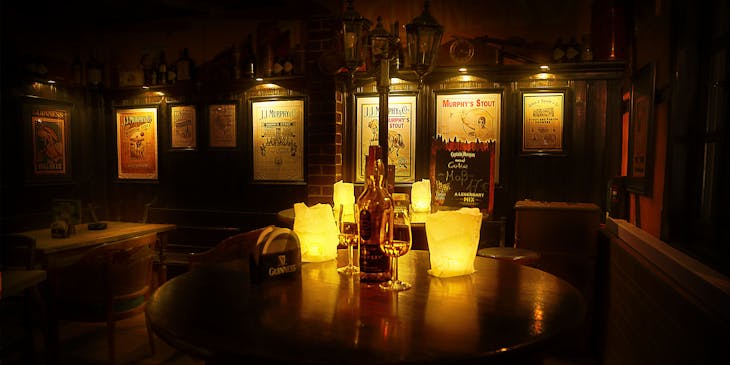Round table in an Irish restaurant with candles, glasses, and an Irish whiskey bottle on top and posters for liquor companies on the walls in the background.