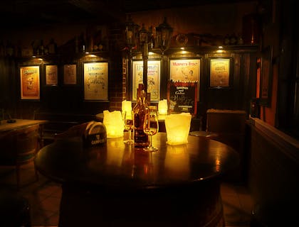 Mesa redonda en un restaurante irlandés con velas, vasos y una botella de whisky irlandés en la parte superior y carteles de compañías de licores en las paredes al fondo.