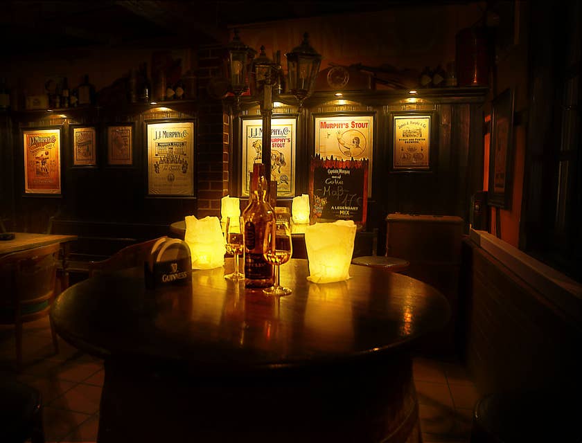 Une table ronde dans un restaurant irlandais avec des bougies, des verres et une bouteille de whisky irlandais sur le dessus et des affiches de marques de spiritueux sur les murs en arrière-plan.