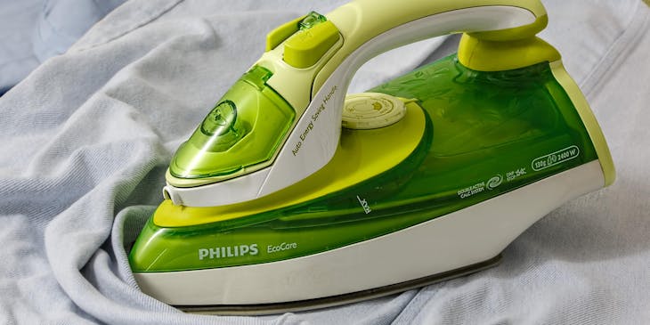 A neon green and white steam iron on a white garment.