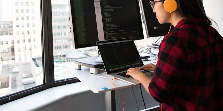 Woman wearing yellow headphones typing on a computer at an IT business.