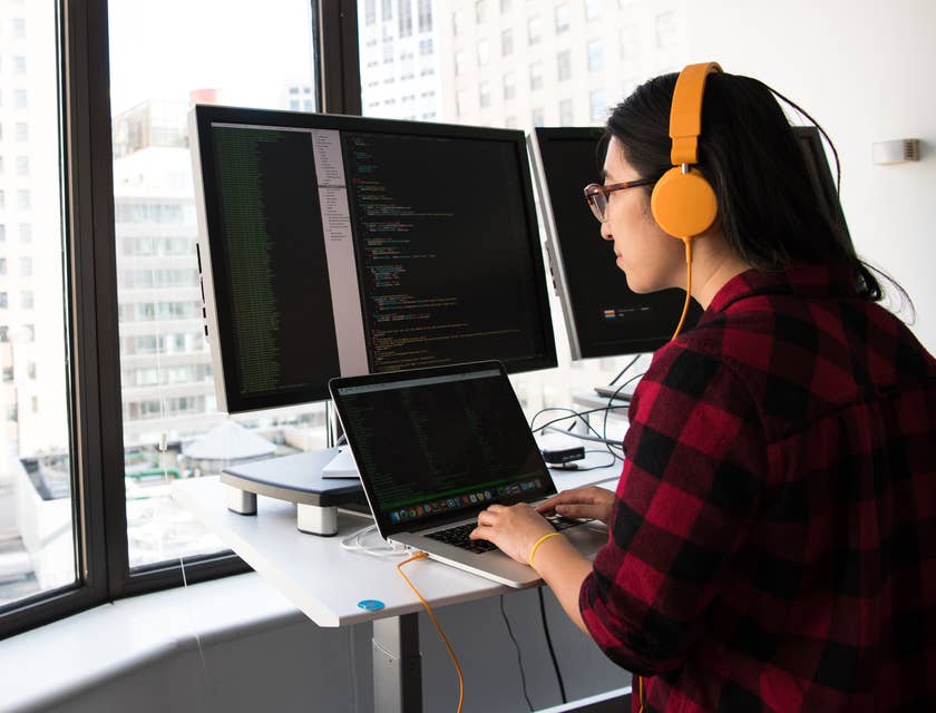 Mulher usando fones de ouvido amarelos digitando em um computador em uma empresa de TI.