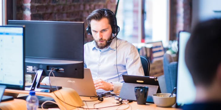 IT support agent wearing headphones and typing on a laptop
