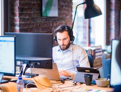 IT support agent wearing headphones and typing on a laptop