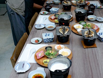 Une table avec bols, poisson grillé et accompagnements divers, au-dessus de laquelle se penche une serveuse.
