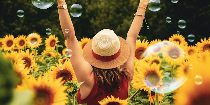 A joyful woman walking through a sunflower field with her arms raised.