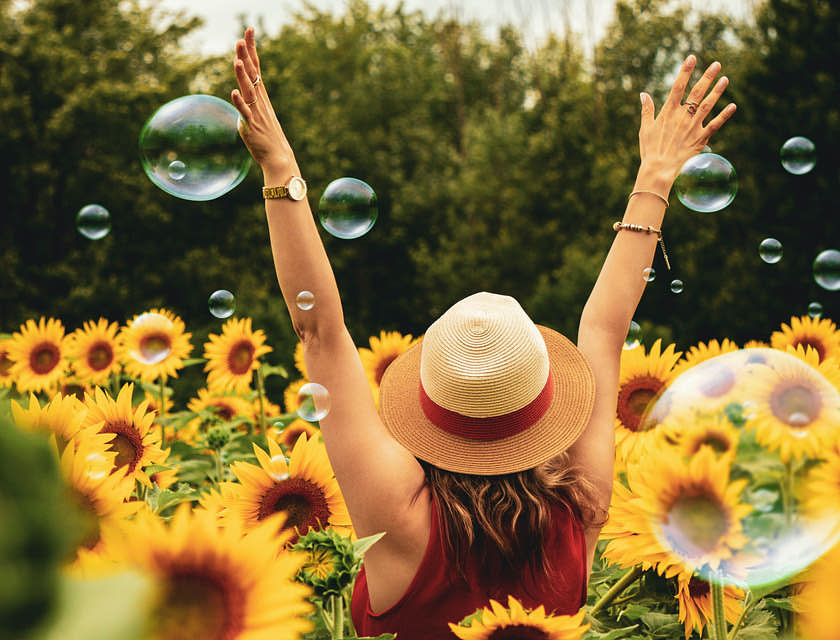 Une femme heureuse marchant dans un champ de tournesols, les bras levés.
