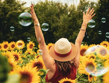 Una mujer alegre caminando por un campo de girasoles con los brazos levantados en un negocio con nombre jubiloso.