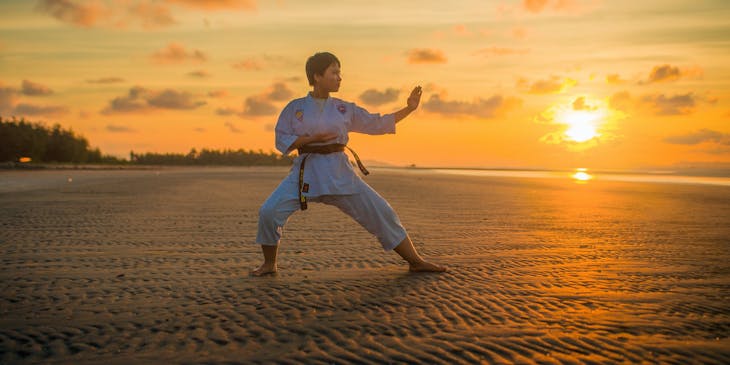 Una donna che fa karate in una spiaggia dopo aver imparato alcune mosse in una palestra di karate.
