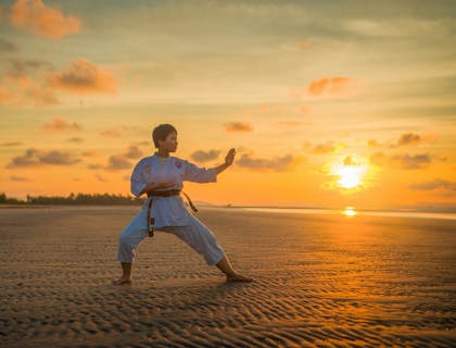A woman doing karate on the beach.