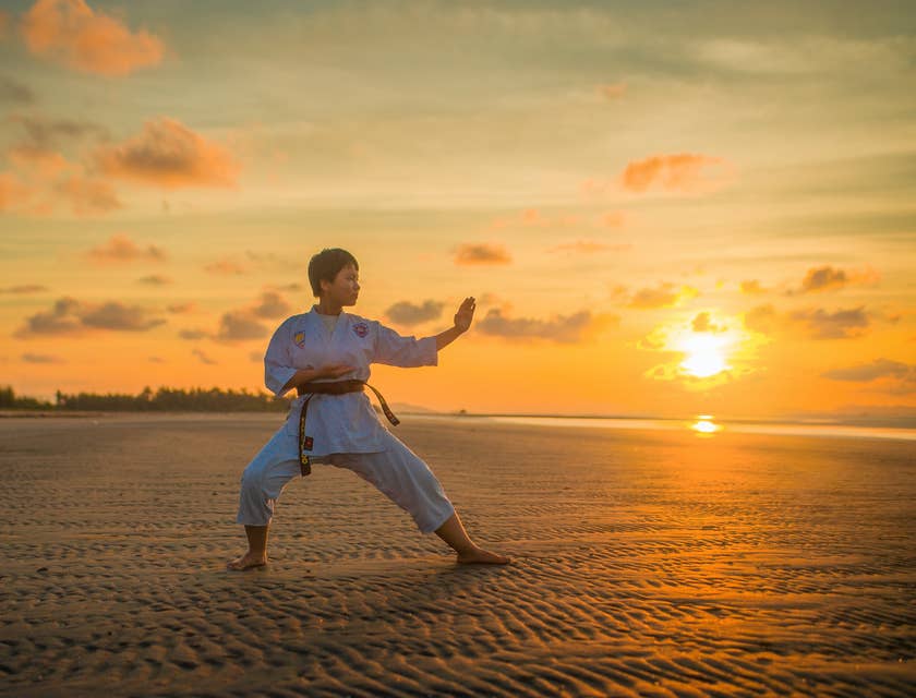 Una donna che fa karate in una spiaggia dopo aver imparato alcune mosse in una palestra di karate.