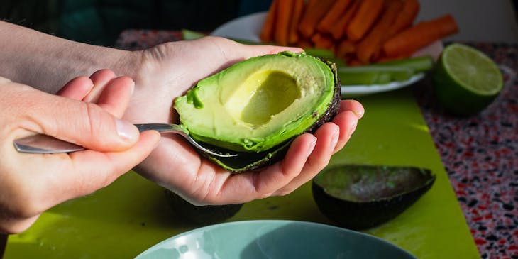 A person scoops an avocado out of its shell