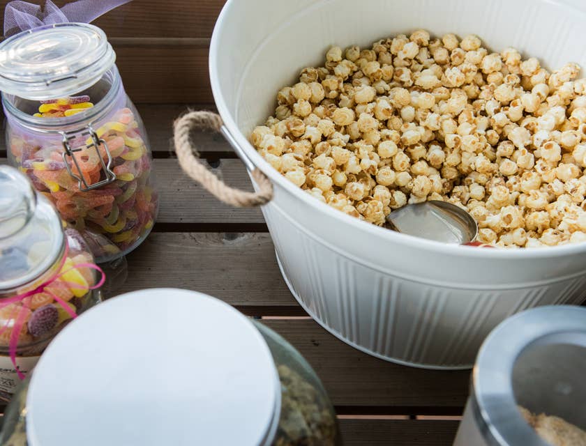 Una ciotola bianca riempita di popcorn dolci affiancata da diversi barattoli pieni di caramelle.