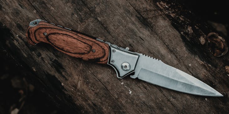 A steel knife with a brown handle on a log.