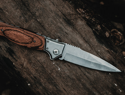 A steel knife with a brown handle on a log.