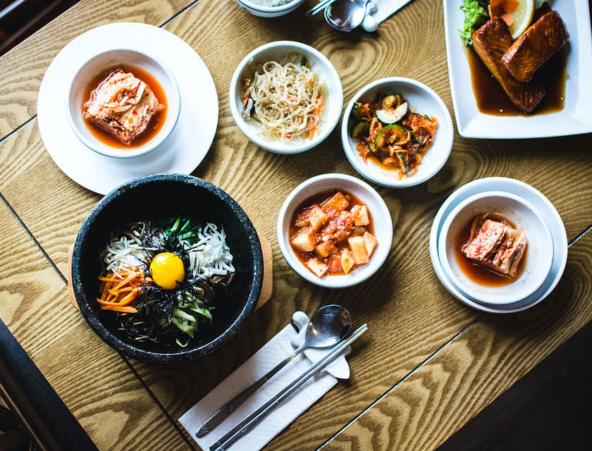 Ein traditionelles Bibimbap mit Kimchi, serviert in verschiedenen Schalen, auf dem Holztisch eines koreanischen Restaurants.
