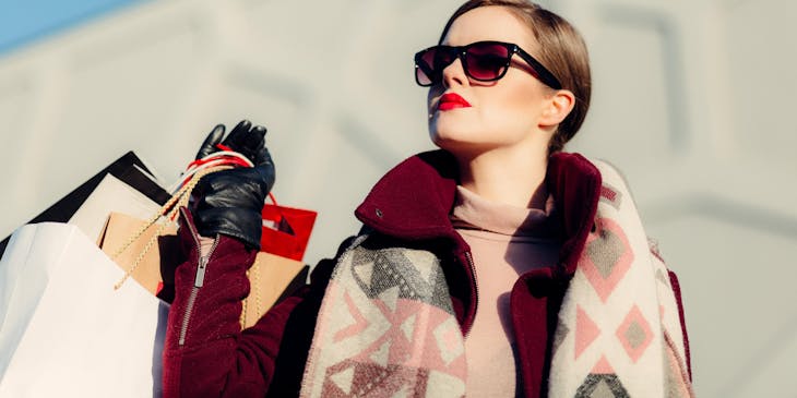 An affluent woman wearing sunglasses and holding shopping bags from lavish businesses.