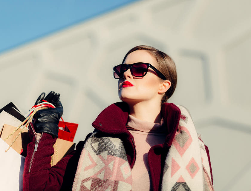 An affluent woman wearing sunglasses and holding shopping bags from lavish businesses.