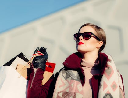 An affluent woman wearing sunglasses and holding shopping bags from lavish businesses.