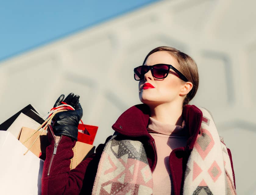 Une femme aisée portant des lunettes de soleil et tenant des sacs de courses provenant de commerces somptueux.