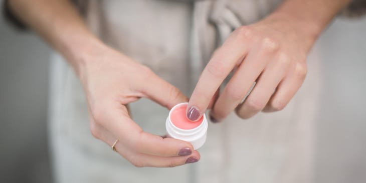 Close-up of a woman's hands holding a small container filled with pink lip balm