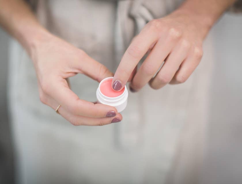 Close-up of a woman's hands holding a small container filled with pink lip balm
