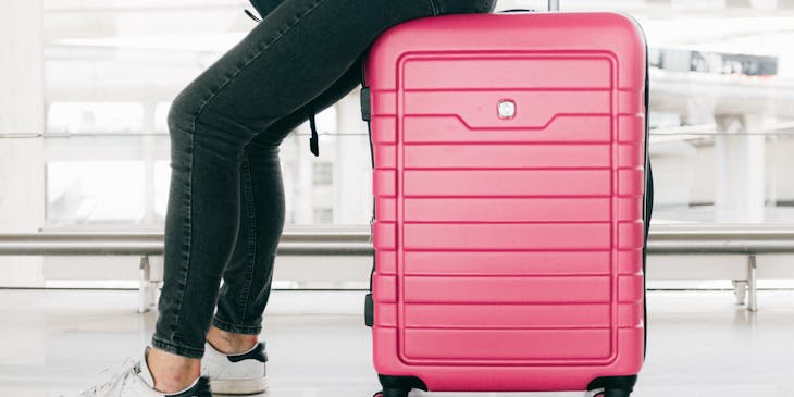 A woman sitting on a pink piece of luggage at an airport.