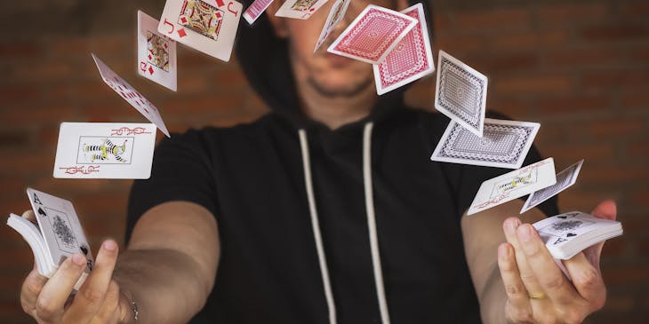 A magician working at a magic shop and flicking playing cards in the air.