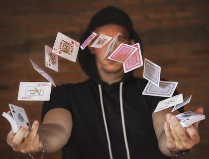 A magician working at a magic shop and flicking playing cards in the air.