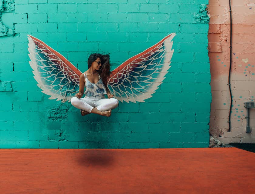 Una donna che sembra sospesa come se volasse magicamente grazie a delle ali dipinte sul muro.