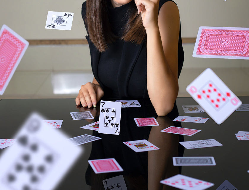 Magician holding card over eye with floating cards around her.