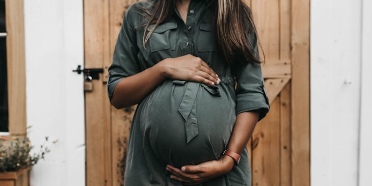 Pregnant woman wearing maternity wear holding stomach.