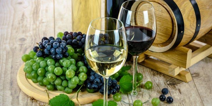 Mature wines in stemmed glasses beside a plate of red and black grapes.