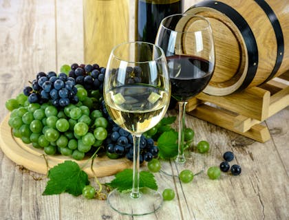 Mature wines in stemmed glasses beside a plate of red and black grapes.