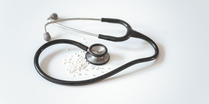 Black and silver stethoscope surrounding small white pills.