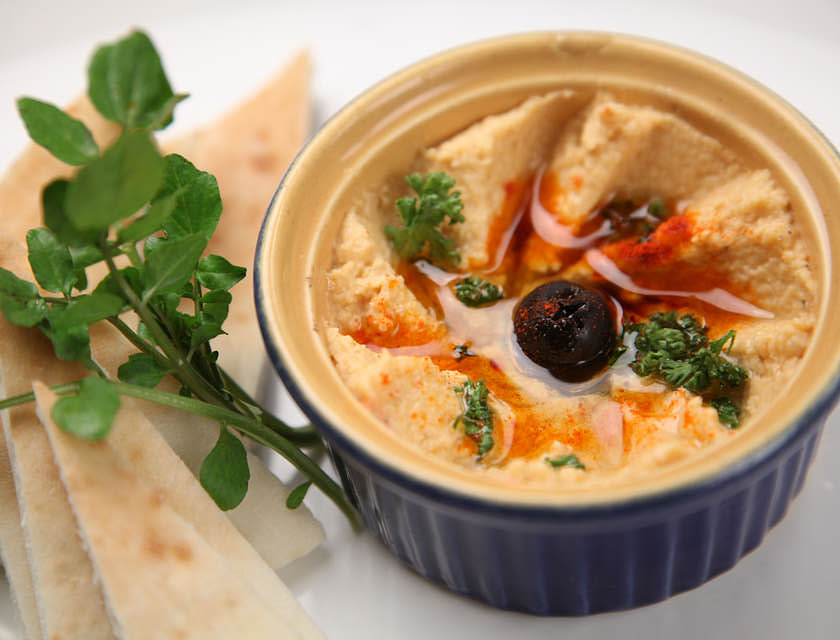 A bowl of hummus beside slices of pita bread being served in a Mediterranean restaurant.