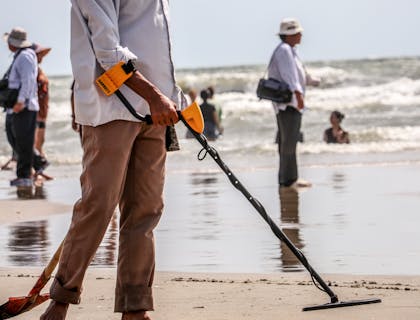 Homem usando um detector de metais em uma praia.