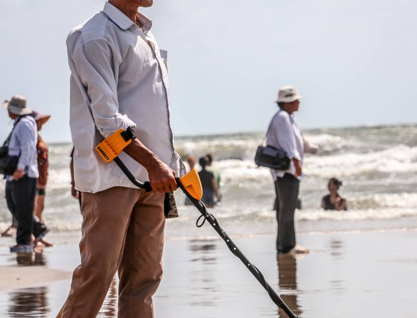 Homem usando um detector de metais em uma praia.