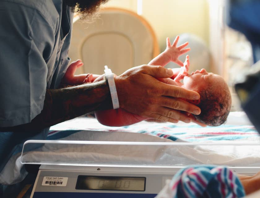 Eine Hebamme hält ein neugeborenes Baby in ihren Händen, um es zu wiegen.