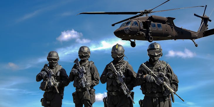 Four armored soldiers from the military carrying rifles with a helicopter in the background.