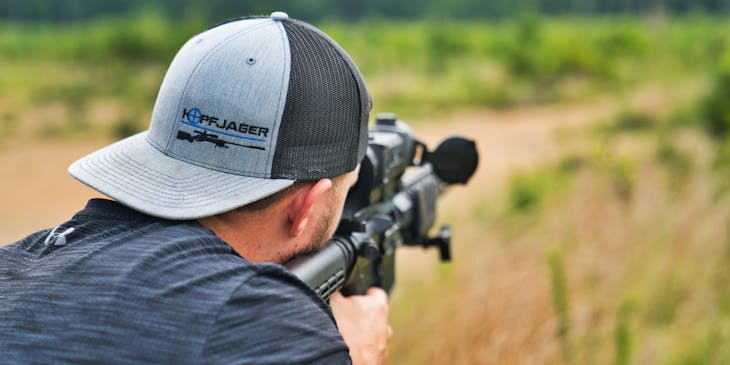 Man in cap taking aim with rifle purchased from a military surplus store.