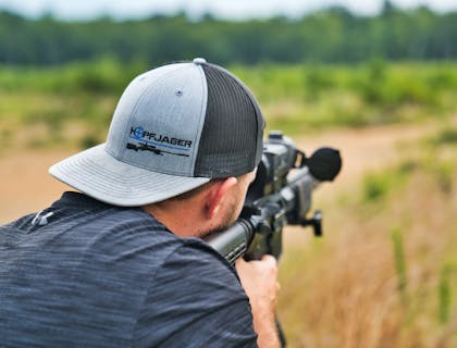 Man in cap taking aim with rifle purchased from a military surplus store.