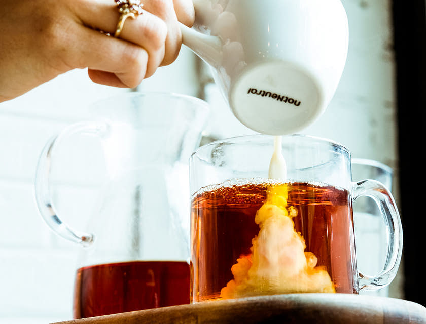 Una persona vertiendo leche en una taza de té en un negocio de té con leche.