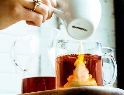 Una persona vertiendo leche en una taza de té en un negocio de té con leche.